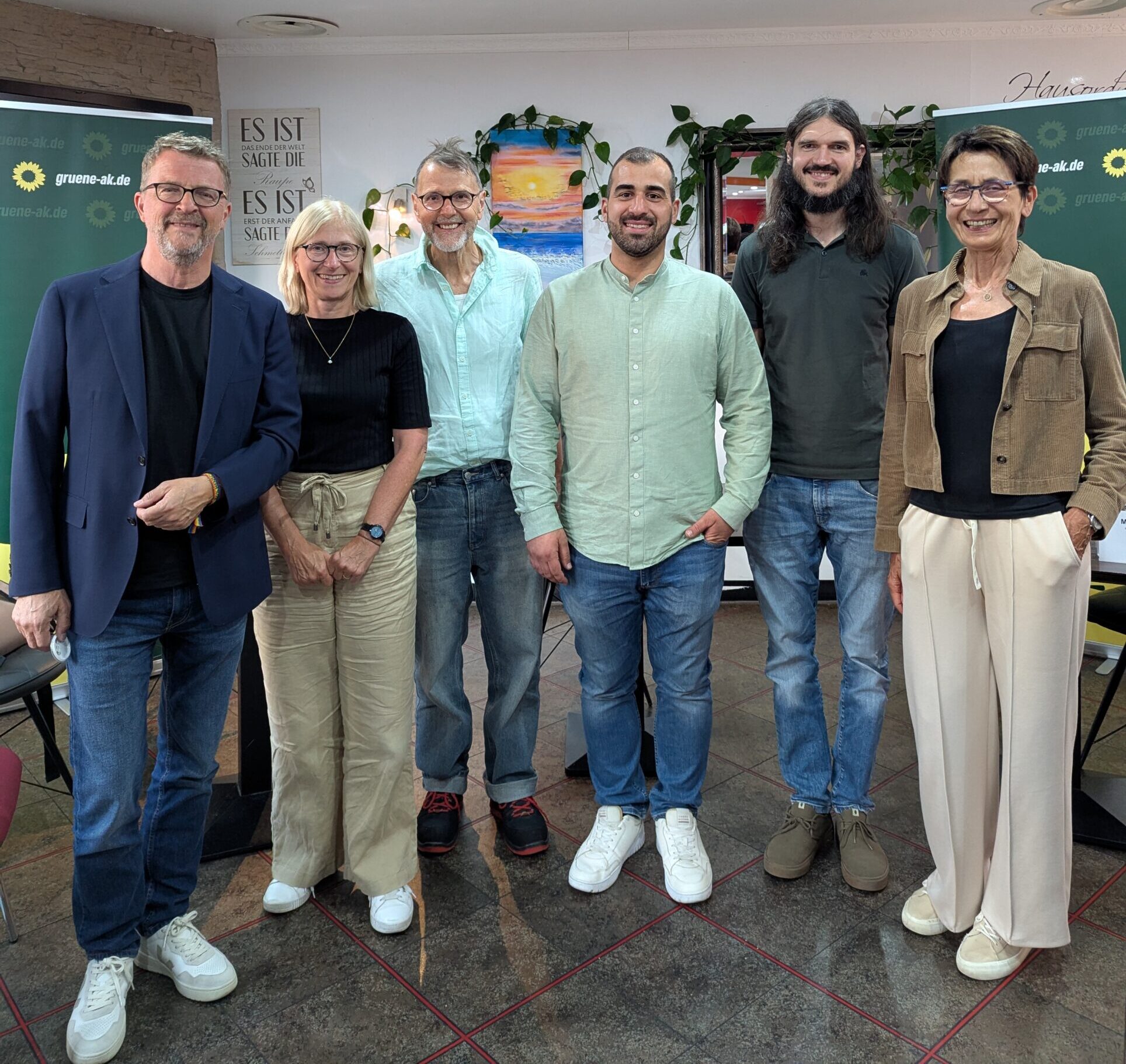 Ein Foto von 6 Personen nebeneinanderstehend: Carl-Bernhard von Heusinger, Elke Richter, Günther Leber, Maurizio Kreis, Manfred Hermann, Susanne Leber. Im Hintergrund sind Banner von den Grünen Kreisverband Altenkirchen aufgestellt.
